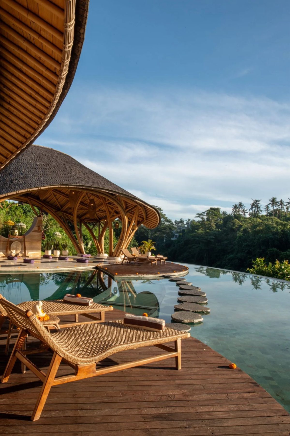 Loungers by an infinity pool with stepping stones and a bamboo pavilion over the jungle
